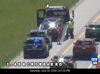 Police car and tow truck on the right shoulder with a person standing between them