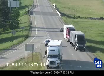 A person in a safety vest is standing near the roadway next to a truck.
