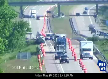 Emergency responders and traffic cones are present on the roadway, indicating an incident.
