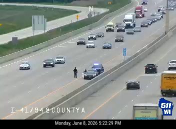 Police car and officers on the shoulder of the highway, traffic is moving.