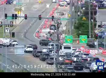 Emergency responders and traffic cones are present on the roadway.